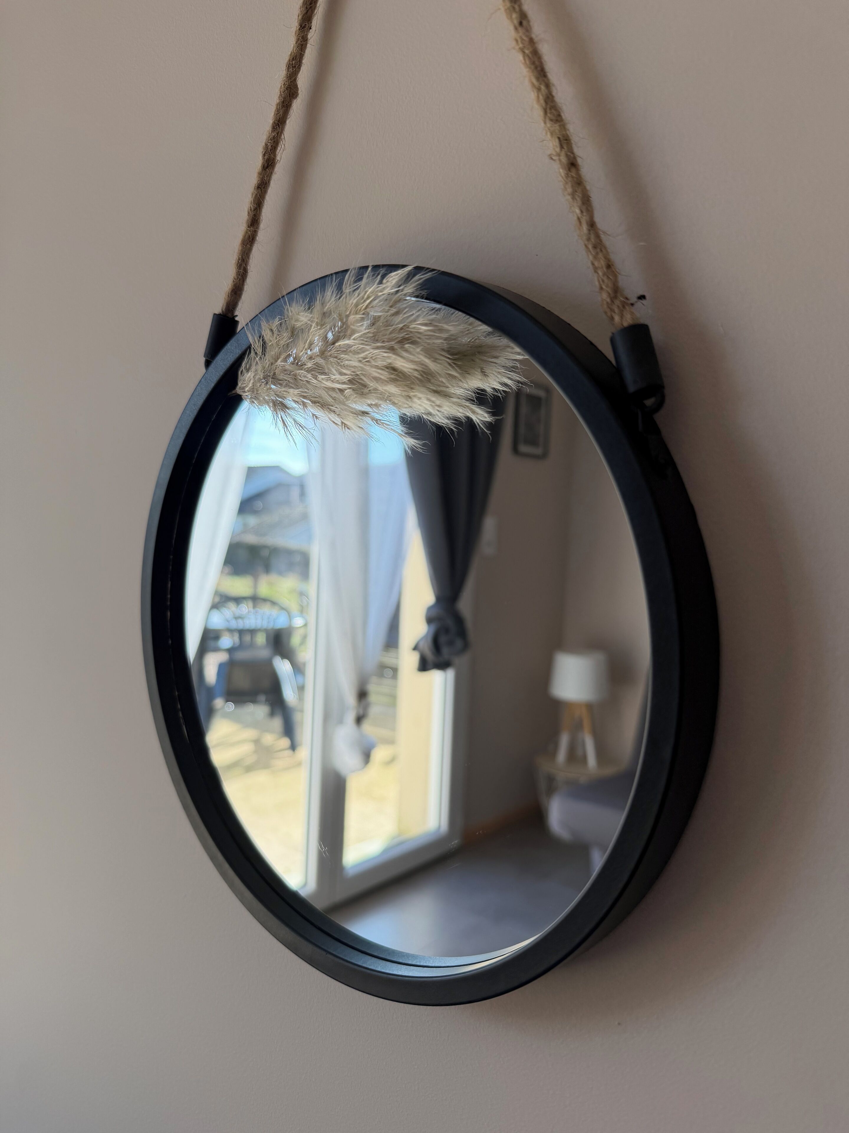 A round mirror with a rope handle, mounted on a wall.