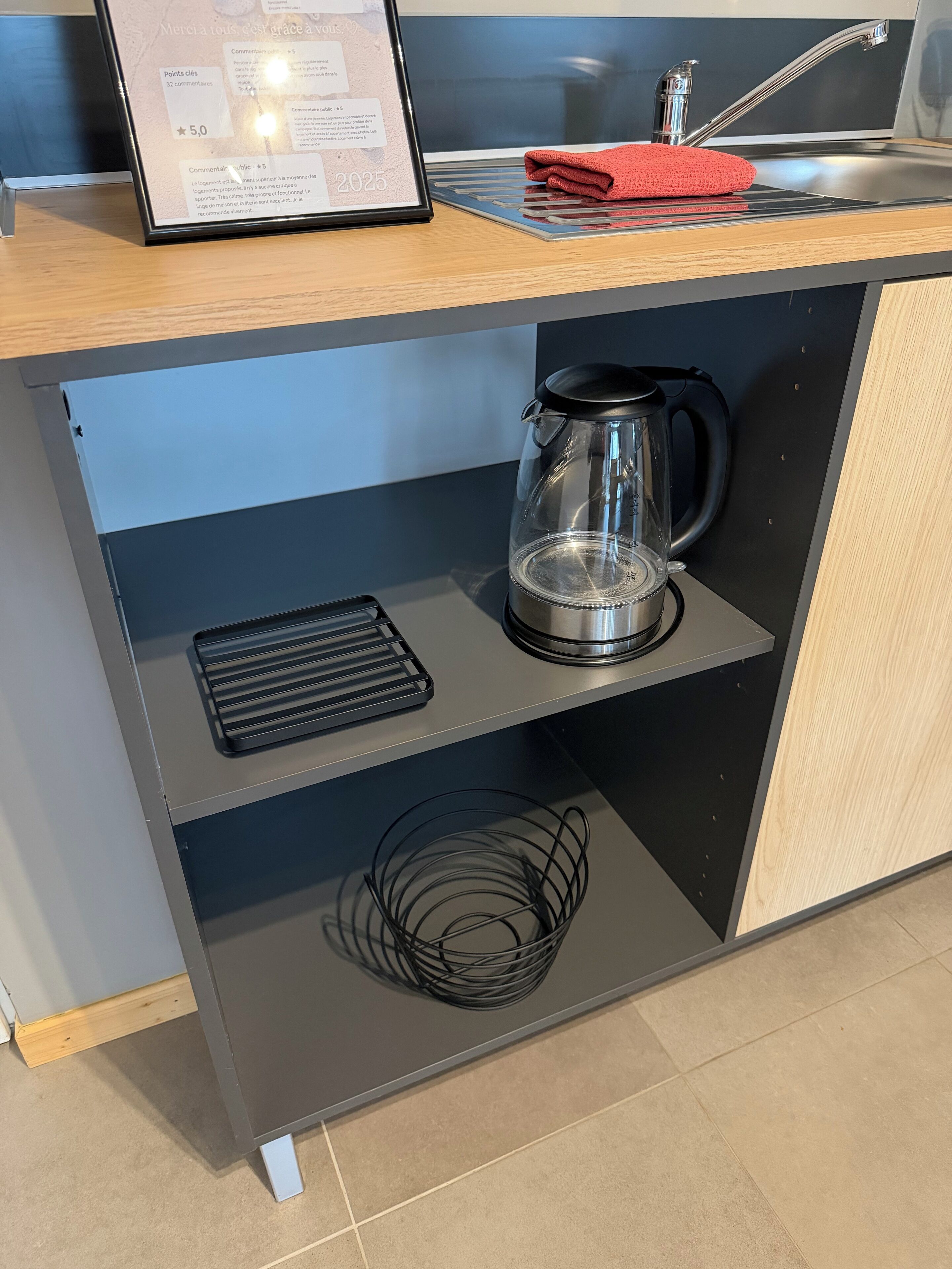 Eine Küche mit integriertem Kaffeeautomaten, einem Wasserkocher und einem Spülbecken mit einem roten Handtuch.