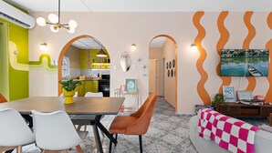 A modern living room with a dining area, featuring a large TV, a sofa with a checkered throw, and a kitchen in the background. - Unique Retro house with pool (Aguadilla)