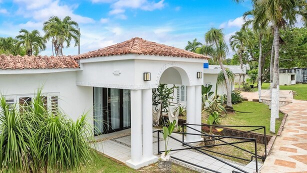 A white building with a tiled roof, a covered entrance, and a garden with palm trees. - Unique Retro house with pool (Aguadilla)