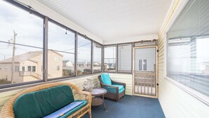A covered balcony with wicker furniture, a small table, and a view of neighboring houses. - New Listing! Walk to Beach, Hot Tub & Games! (Kill Devil Hills)