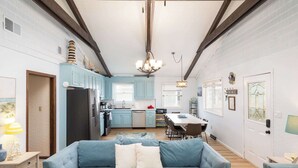 A modern kitchen with light blue cabinets, a central island, and a dining area with a table and chairs. - New Listing! Walk to Beach, Hot Tub & Games! (Kill Devil Hills)