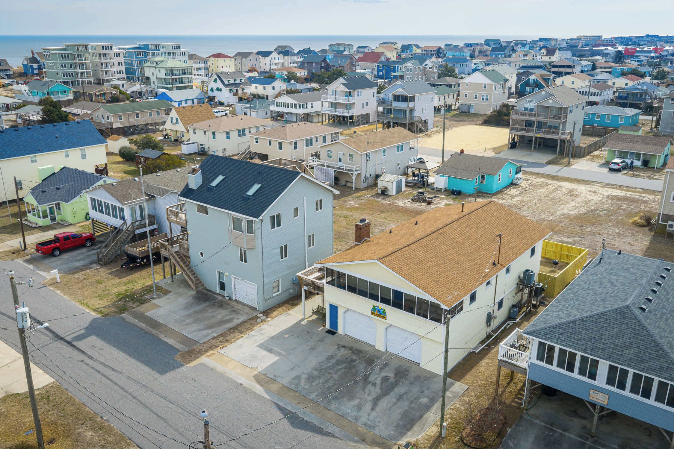 A residential area with houses, a street, and a beach in the background.