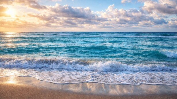 Une plage avec des vagues, un ciel dégagé et des nuages.