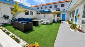 Une cour avec une pelouse artificielle, un canapé, une table et un parasol bleu.