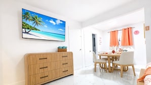 Una habitación luminosa con un armario de madera, una mesa de comedor con sillas y un cuadro de una playa.