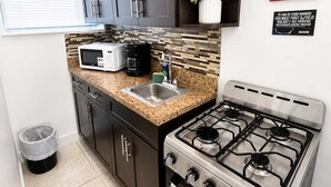Cozinha compacta com armários escuros, micro-ondas, máquina de café, pia e fogão a gás.