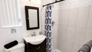 Casa de banho com sanita, lavatório, chuveiro e barra de toalhas.