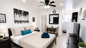 Quarto moderno com cama, mesas de cabeceira, escrivaninha, cadeira, televisão e ventilador de teto.