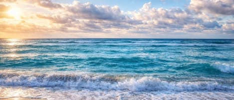 Une plage avec des vagues, un ciel dégagé et des nuages.