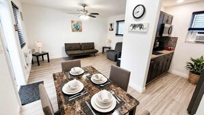 Ein modernes Wohnzimmer mit Essbereich, einer Couch, einem Deckenventilator und einer Küche mit Schränken und einer Mikrowelle.