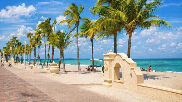 A beach with palm trees, a paved walkway, and a stone archway. - Hollywood Beach Suites - Steps to the Beach & Family Fun! (Hollywood)