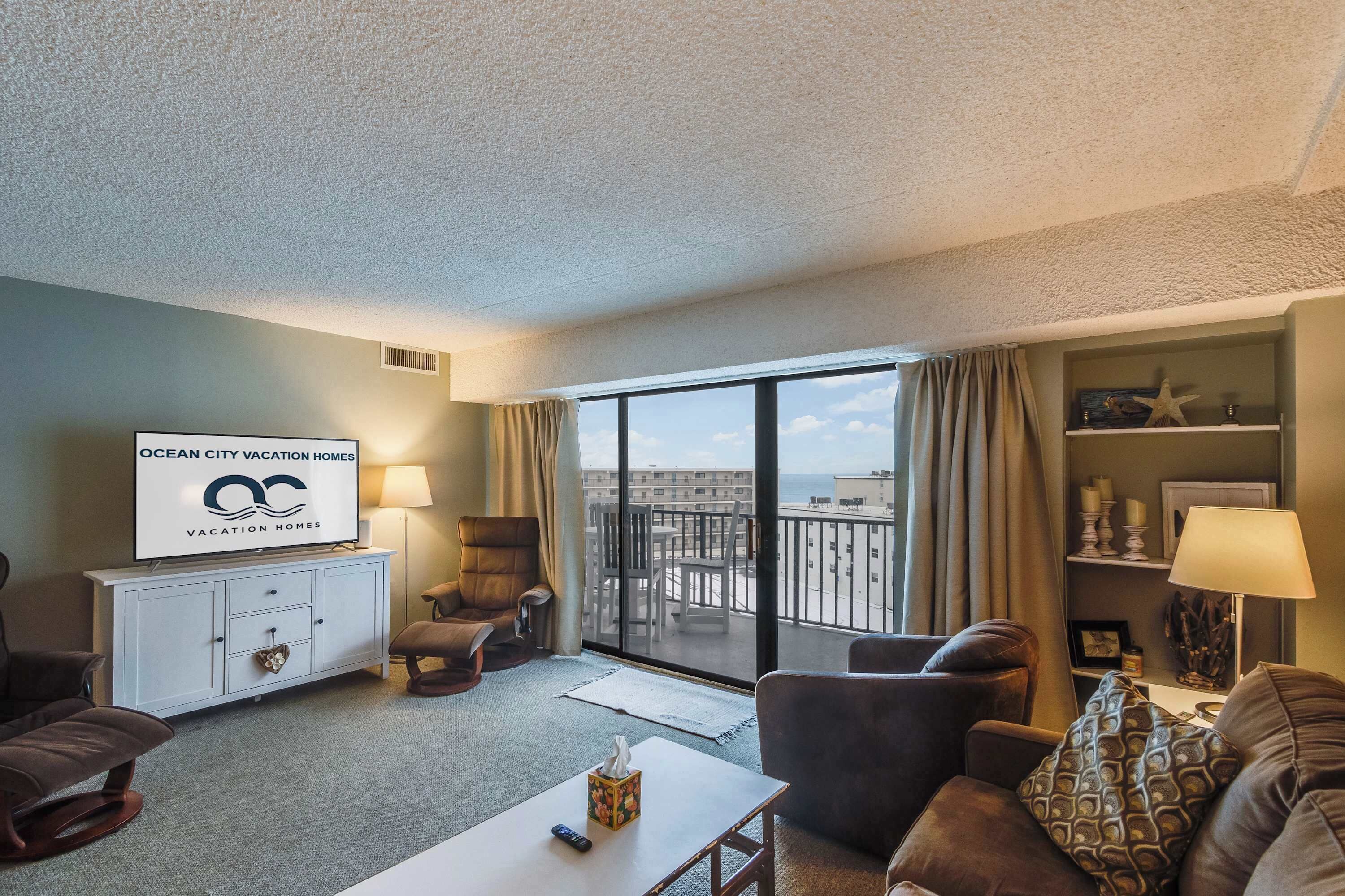 Habitación de hotel con balcón, televisión de pantalla plana, sofá, mesa de centro y mesita de noche con lámpara.