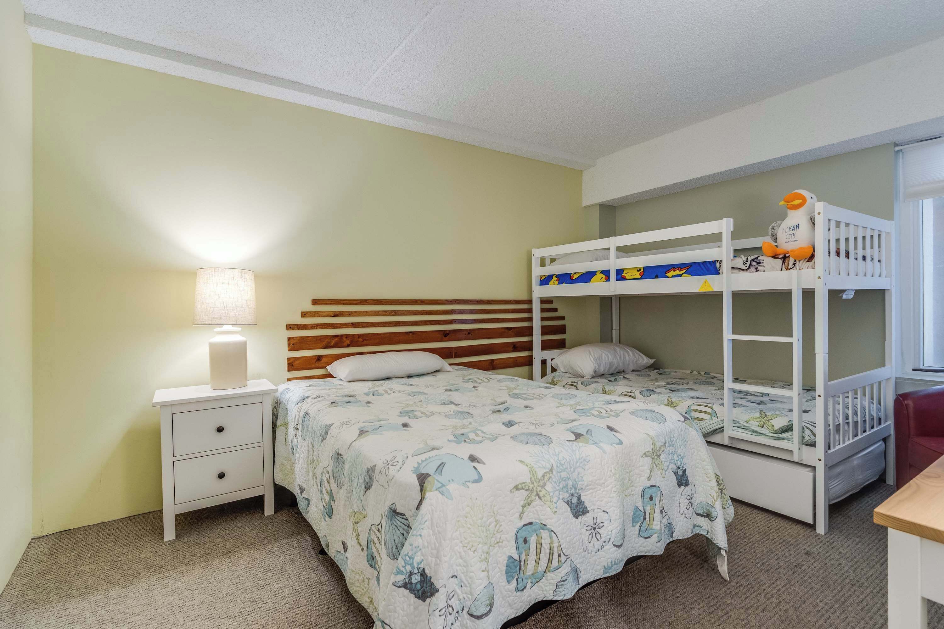 A room with bunk beds, a nightstand with a lamp, and a bed with a patterned bedspread.