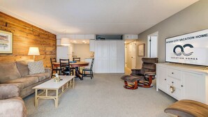 Ein gemütliches Wohnzimmer mit einer Wand aus Holzpaneelen, einem Essbereich und einem Fernseher, der "Ocean City Vacation Homes" anzeigt.