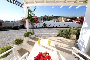 Una terrazza con tavolo e sedie, piante in vaso e due bicchieri di succo d'arancia.