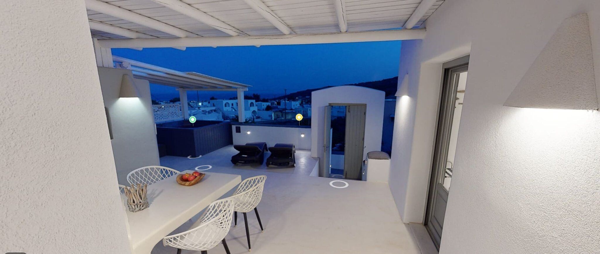 Terraza en la azotea con zona de comedor, dos sillones de relax y vistas a la ciudad al anochecer.