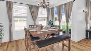 A dining area with a wooden table set for four, a bench, and a view of a garden through large windows. - Paso del Sol |Pool Table, fire pit (Paso Robles)