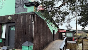 A rustic wooden building with a green exterior, a sign reading "KRUSOVI PIVOL," and a sign for "NA PASTVINACH." - Hotel Na Pastvinách (Tremesne)