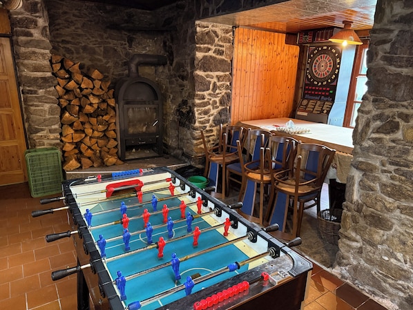 A room with a foosball table, a dartboard, and a fireplace.