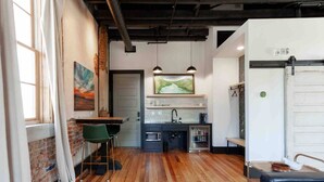 A modern kitchen with a bar area, wooden flooring, and hanging pendant lights. - Romantic Historic Loft on Main Street (Heber Springs)