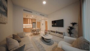 A modern living room with a sofa, coffee table, and TV. - Dubai Hills Apt with Infinity Pool (Dubai)