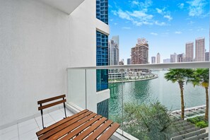 Ein Balkon mit einer hölzernen Bank, einer weißen Wand und Blick auf eine Stadtlandschaft sowie ein Gewässer.