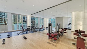 Academia moderna com grandes janelas, piso de madeira e diversos equipamentos de exercício.