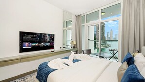 Quarto de hotel com uma cama grande, televisão de tela plana na parede, varanda com vista para a cidade e uma pequena mesa com uma cadeira.
