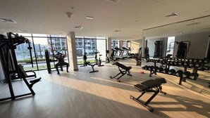 Ein Fitnessstudio mit unterschiedlichen Trainingsgeräten, großen Fenstern und einer Spiegelwand.
