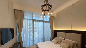 Ein modernes Hotelzimmer mit einem großen Bett, einem Flachbildfernseher, einem Holztisch und Blick auf die Stadt durch große Fenster.