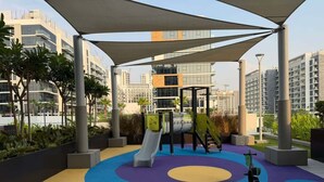 Ein Spielplatz mit Rutsche und Trainingsgeräten, umgeben von bunten, kreisförmigen Mustern auf dem Boden und einem darüberliegenden Baldachin.