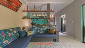 Een woonkamer met een blauwe bank, decoratieve schappen en een keuken in de achtergrond.