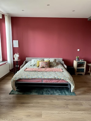 Une chambre à coucher avec un lit, une table de chevet, une petite table et une fenêtre avec des rideaux.