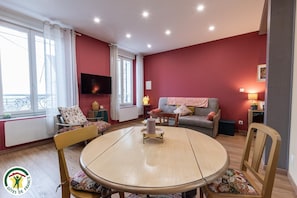 Un salon chaleureux avec une table ronde en bois, un canapé et un téléviseur fixé au mur.
