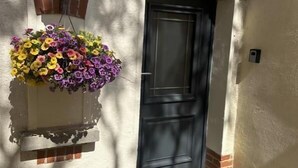 Un bâtiment avec une porte noire, une jardinière suspendue et une petite fenêtre.