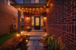 A brick house with a front porch, string lights, and a door with glass panels. - Game Room Getaway + Cozy Retreat Near Blue Mtn Ski Resort, Golf & Spa FREE Park (Collingwood)