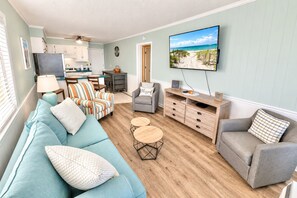 A living room with a sofa, armchairs, a coffee table, and a TV mounted on the wall. - Ocean View 2BR + Steps from the Beach + Pool (Myrtle Beach)