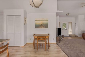 Ein Essbereich mit Holztisch und Stühlen, einem Bild an der Wand und einem Gang zu einem weiteren Raum.