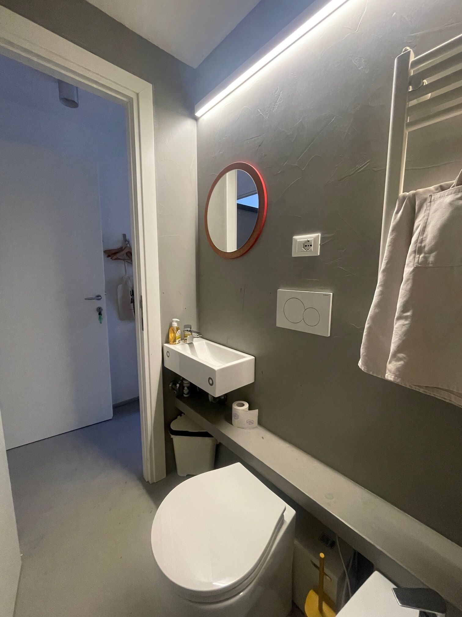 Une salle de bain moderne avec des toilettes blanches, un lavabo surmonté d’un miroir et une serviette suspendue à un porte-serviettes.