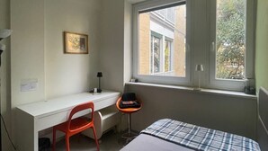 Un dormitorio con cama, escritorio, silla, ventana y ventilador de techo.