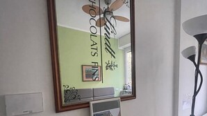 Una habitación con un espejo grande en la pared, un cuadro enmarcado debajo y una mesita con otro cuadro enmarcado encima.