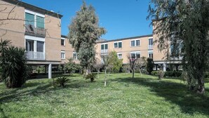Un patio con césped, árboles y un edificio de varios pisos con balcones.