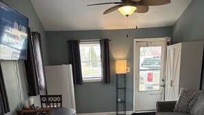 A living room with a TV, a ceiling fan, a sofa, a coffee table, and a rug. - Quaint Studio Unit in fantastic Beecher with refreshing AC (Beecher)