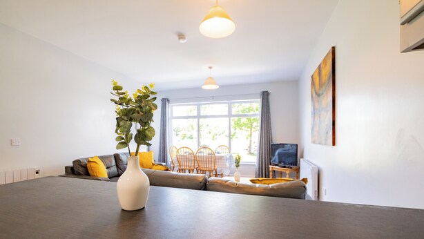 A modern living room with a sofa, a dining table, and a large window. - Great-Value Galway Apartment for Groups (Galway)