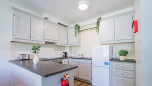 A modern kitchen with white cabinets, a built-in island, a toaster, a refrigerator, and a fire extinguisher. - Great-Value Galway Apartment for Groups (Galway)