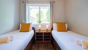 A twin room with two beds, a small table with lamps, a window with curtains, and a plant on the windowsill. - Great-Value Galway Apartment for Groups (Galway)