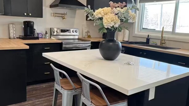 A modern kitchen with dark cabinetry, a white island, and two bar stools.