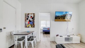 A room with a dining table, chairs, a bed with a blue and white patterned bedspread, a TV mounted on the wall, and a white storage unit. - South Beach 2BR Condo Walk to Beach  (Miami Beach)