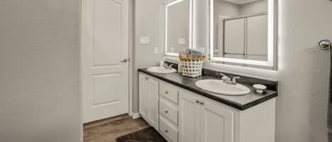 A bathroom with white cabinets, two sinks, and a large mirror.